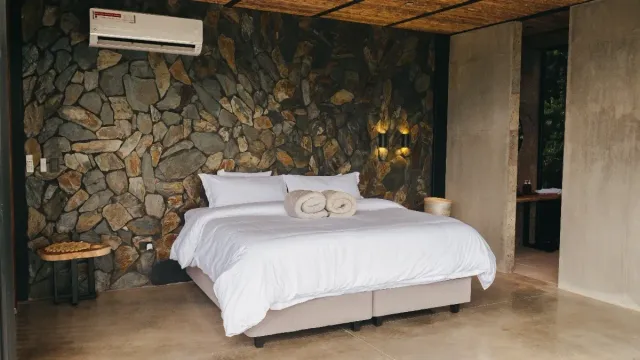 Habitación de lujo en glamping Bucaramanga con cama king y pared decorativa en piedra natural.