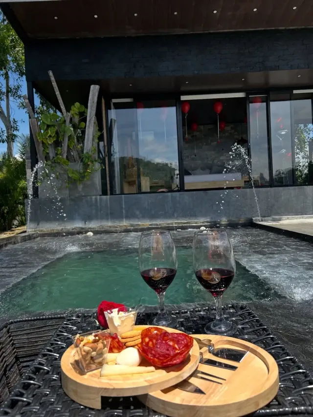 Jacuzzi privado al aire libre con tabla de quesos y vino frente a cabaña, experiencia de glamping para parejas en ambiente romántico.