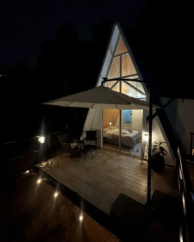 Cabaña tipo A-frame iluminada de noche con terraza y vista al bosque en glamping Bucaramanga.