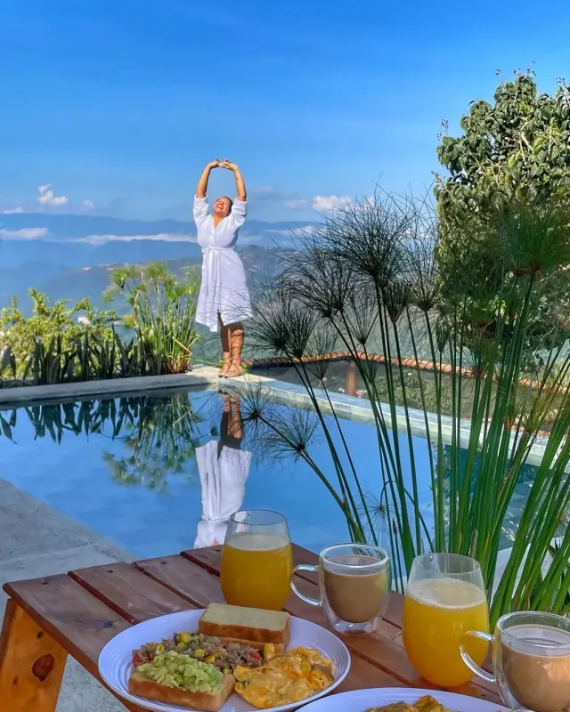 Desayuno servido junto a piscina con mujer disfrutando la vista montañosa en glamping Bucaramanga.