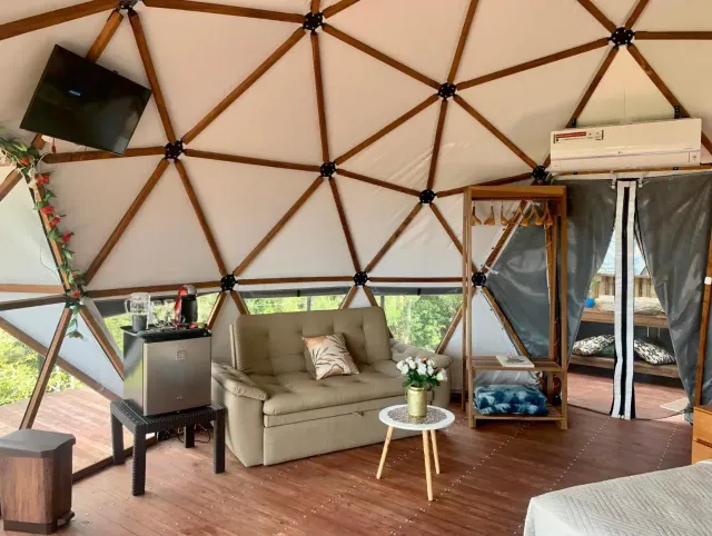 Interior de domo geodésico con sofá, minibar y vista natural en glamping Bucaramanga.