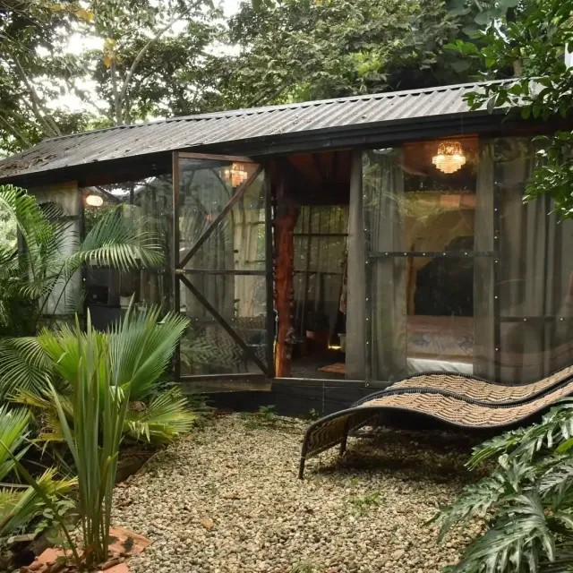 Cabaña estilo glamping rodeada de vegetación con zona exterior y silla reclinable, ideal para una experiencia de alojamiento natural.