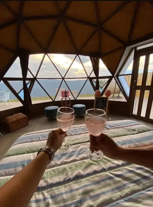 Brindis en domo de glamping santander con vista a montañas en San Gil y ventanales triangulares, ambiente íntimo.