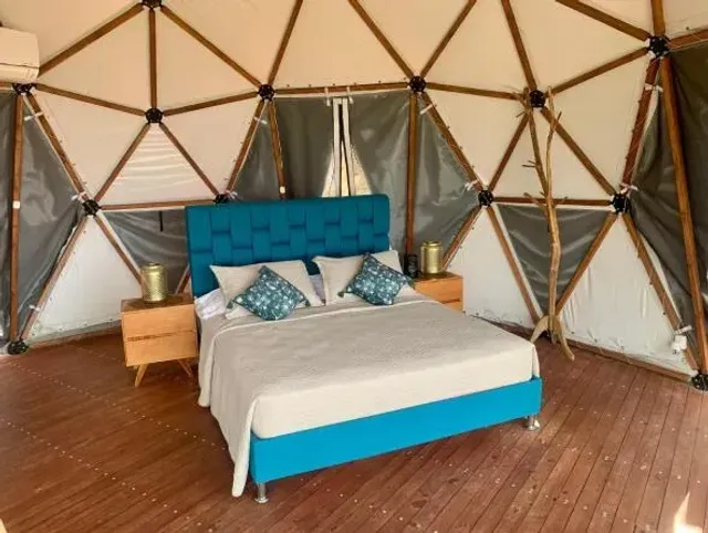 Cama doble con cabecero azul y decoración moderna en domo de glamping Bucaramanga.
