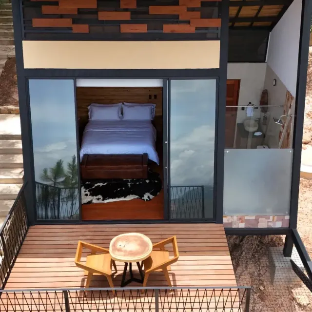 Cabaña moderna elevada con terraza y mural artístico, rodeada de árboles, experiencia de glamping moderno en la naturaleza.