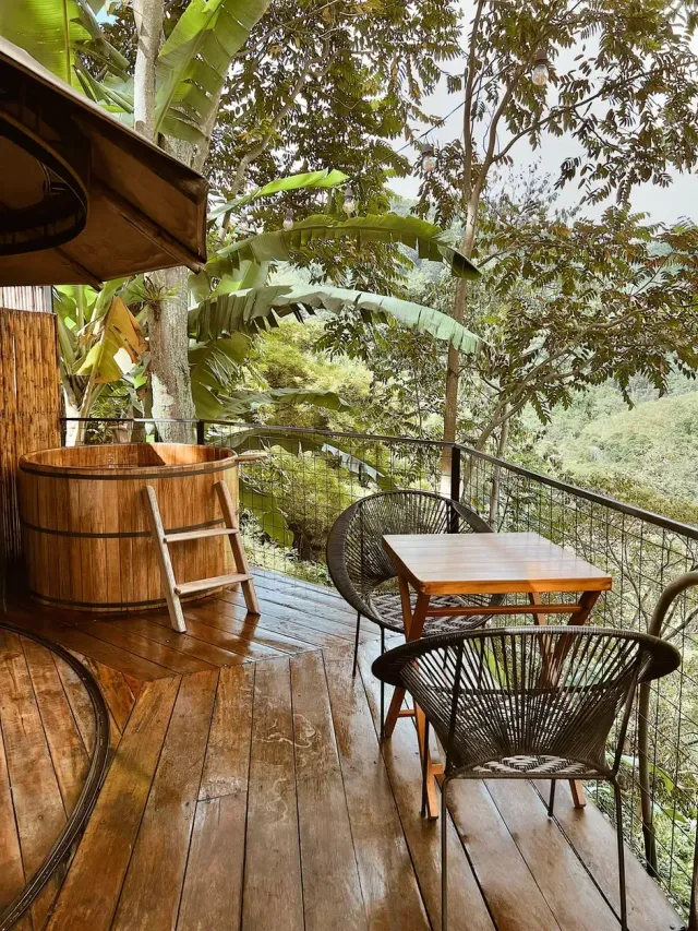 Terraza con tina de madera, sillas y vista panorámica al bosque en glamping de lujo.