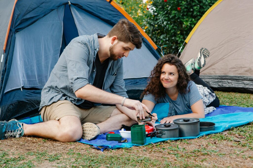 Pareja acampando, preparando comida juntos frente a una tienda de campaña