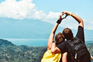 Pareja haciendo un corazón con las manos frente a un paisaje natural.