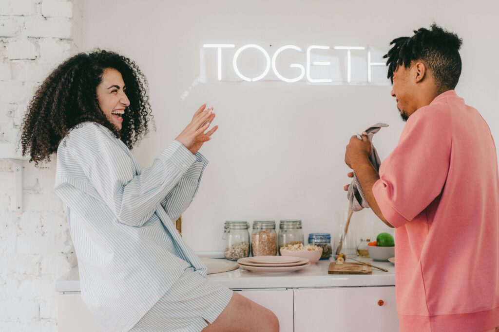 Pareja disfrutando de un momento divertido en la cocina, con la palabra 'Together' iluminada en la pared