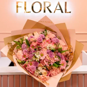 Ramo de flores en tonos rosados y lilas con delicados detalles, presentado frente a un letrero elegante de "Floral".