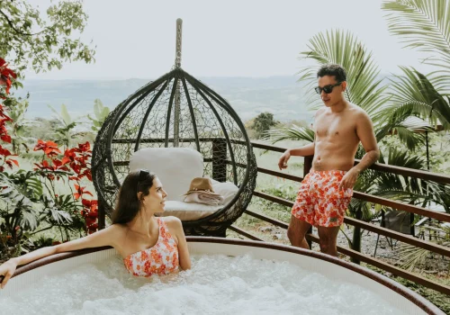 Una pareja disfruta de un jacuzzi rodeado de vegetación tropical y vistas panorámicas. La escena transmite relajación y lujo, ideal para promocionar servicios de spa, escapadas románticas o alojamientos boutique con experiencias exclusivas.